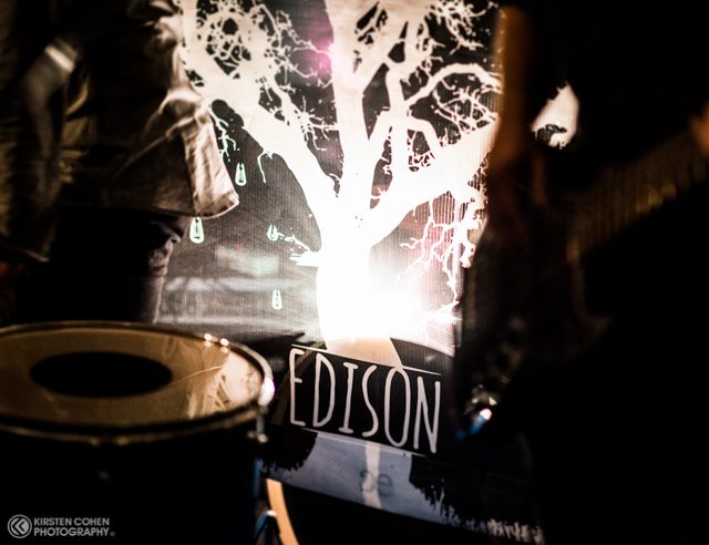 Band performance with drum and illuminated backdrop.