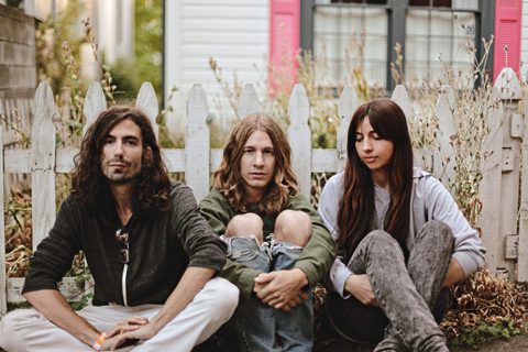 Three people sitting by a white fence.