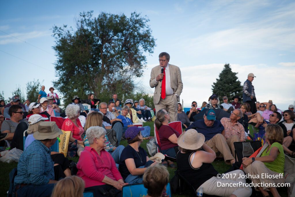 Outdoor gathering with speaker addressing seated crowd.
