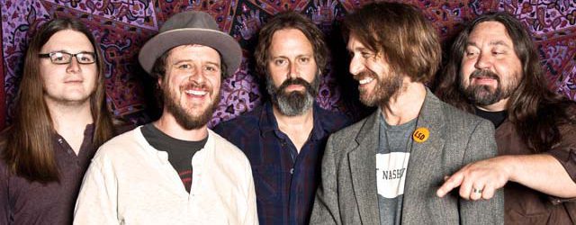 Five men smiling in front of patterned backdrop.