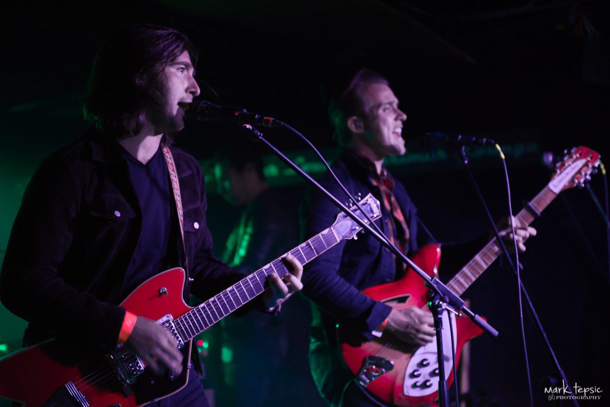 Musicians performing with guitars on stage.