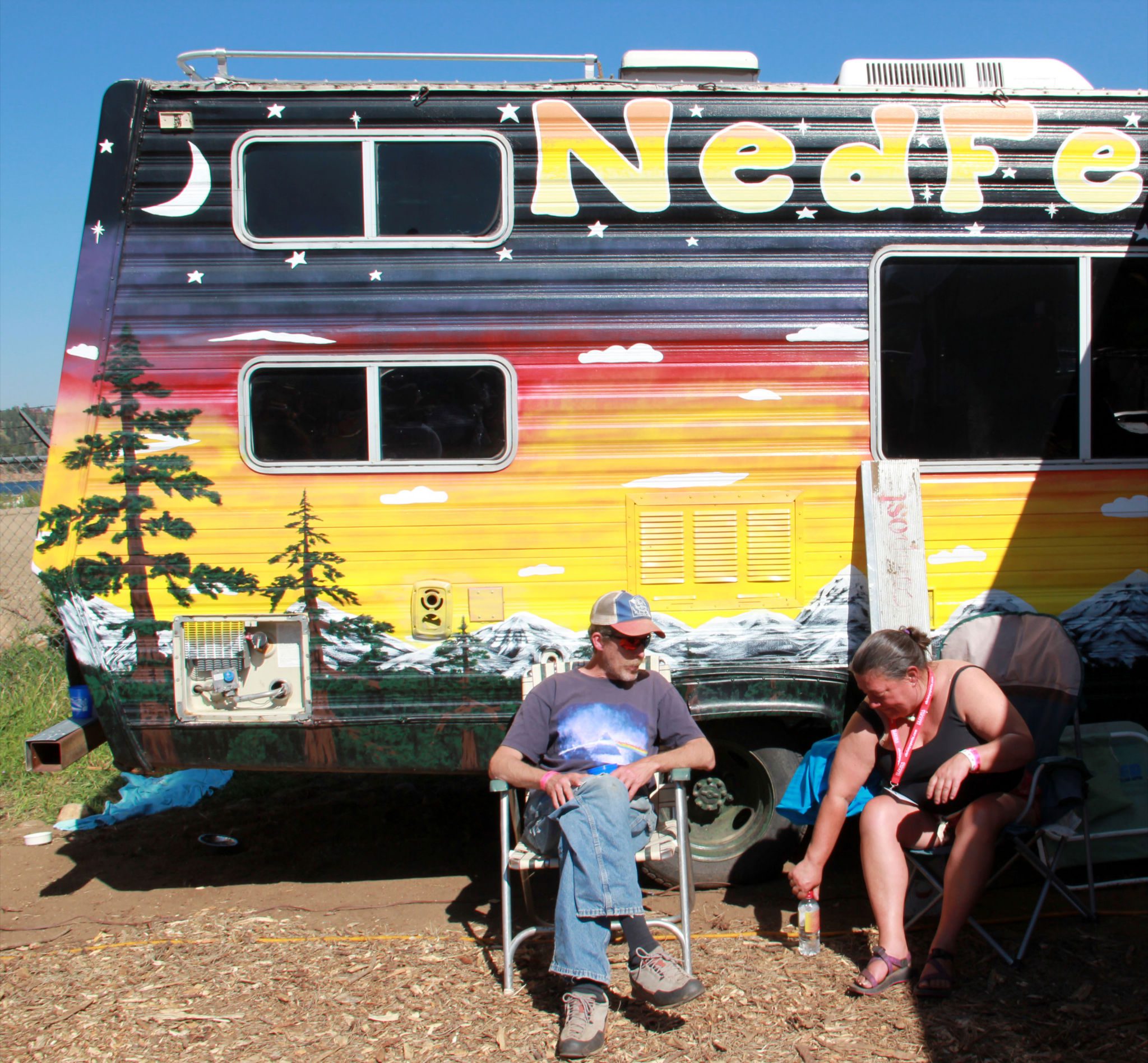 Colorful camper with two people sitting outside.