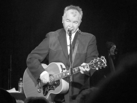 Musician performing with acoustic guitar on stage.