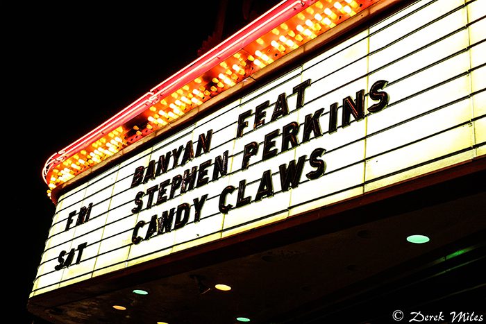 Theater marquee displaying concert information at night.