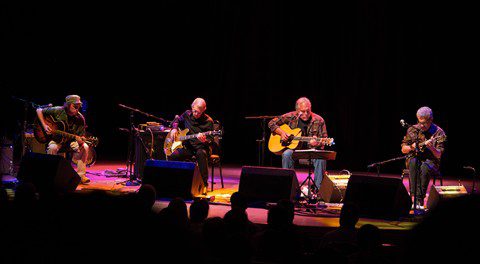 Band performing on stage with guitars, seated.