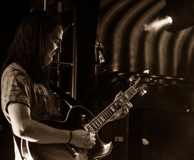 Guitarist playing on stage under spotlight.