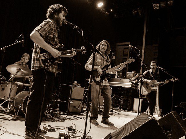 Band performing live on stage in sepia.