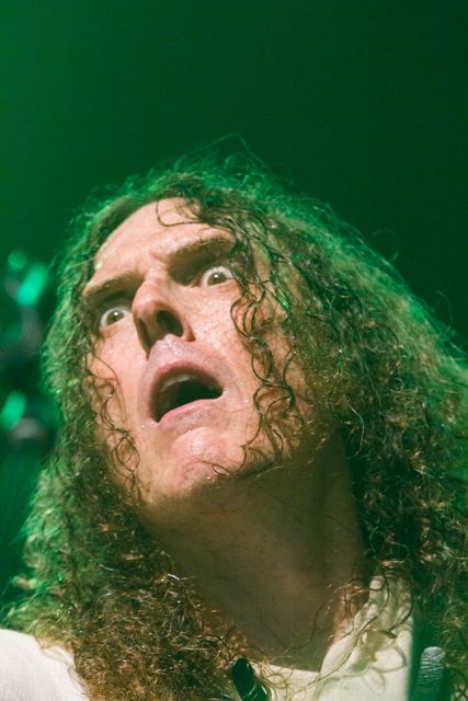 Man with long hair looking surprised, green lighting.