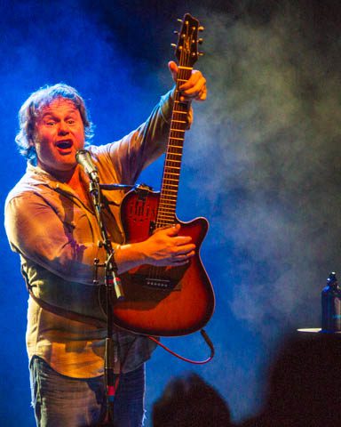 Musician energetically playing guitar on stage.