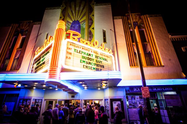 Neon-lit theater entrance with crowd at night.