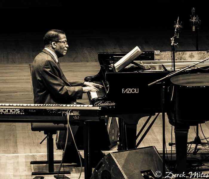 Man playing piano on stage, black-and-white.