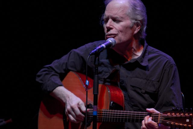 Singer performing with guitar on stage.