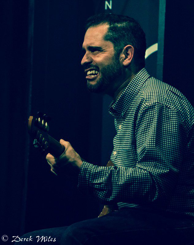 Man playing guitar, smiling on stage.