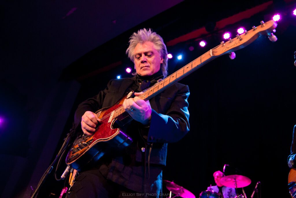 Musician playing guitar on stage with lights.
