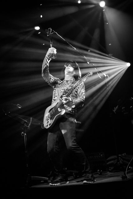 Guitarist performing energetically on stage, black-and-white.