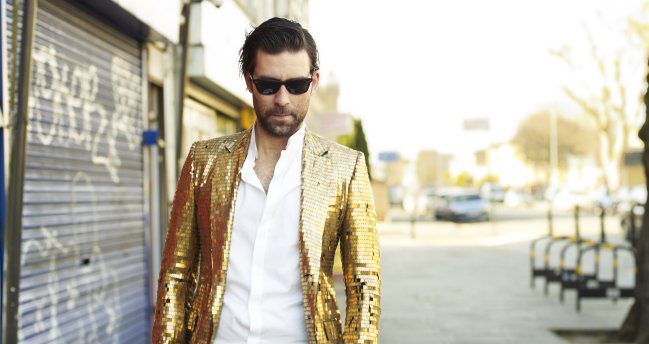 Man in gold jacket and sunglasses walking.