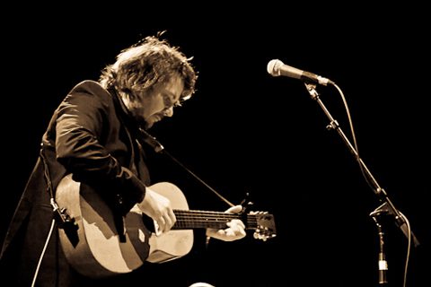 Musician playing acoustic guitar on stage.
