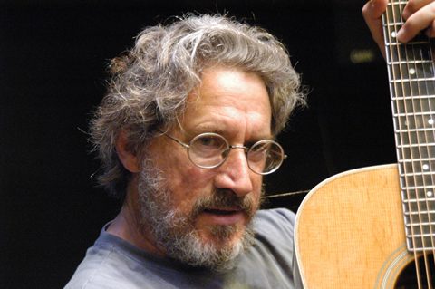 Man holding a guitar, wearing glasses.