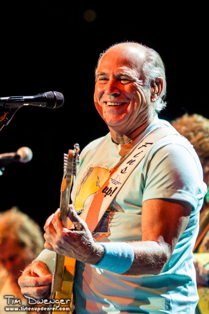 Man playing guitar on stage, smiling brightly.
