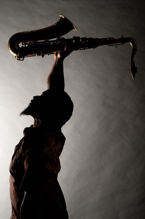 Silhouette of person holding saxophone overhead.