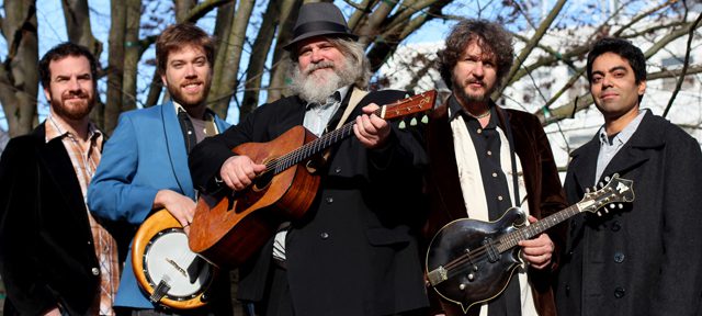 Five musicians posing with instruments outdoors.