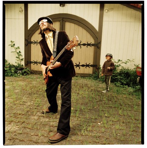 Man playing guitar outside, child in background.
