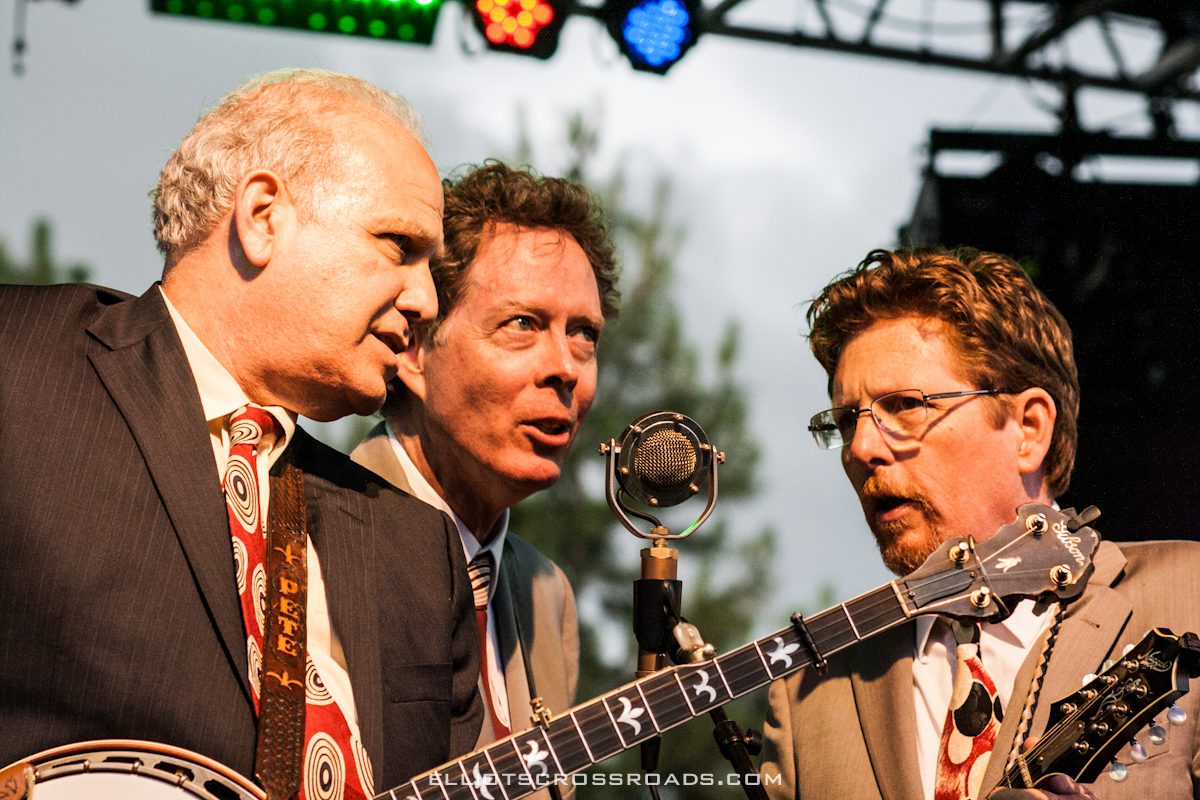 Three musicians performing with banjos on stage.