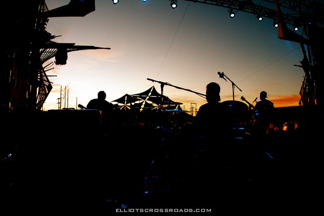 Silhouetted band performing at outdoor festival.