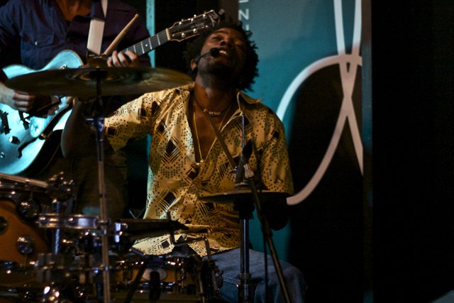 Musician passionately playing drums and guitar onstage.
