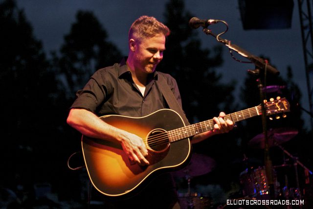 Musician playing guitar on stage at night.
