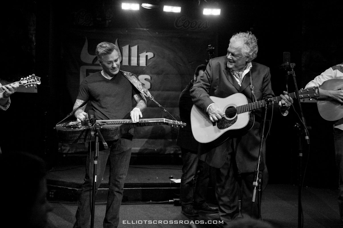 Musicians playing guitars on stage, smiling, performing.