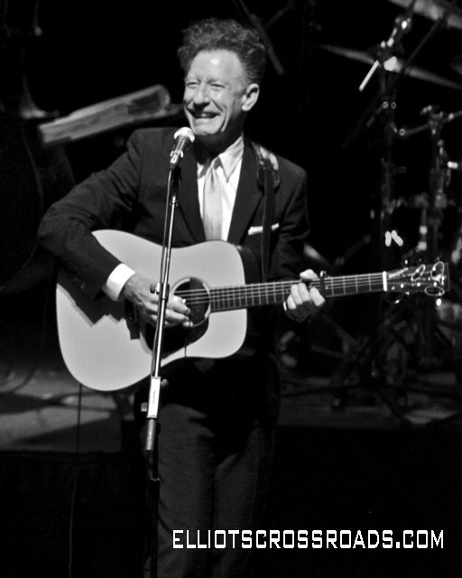 Man playing guitar on stage, smiling.