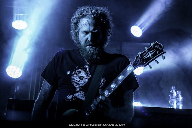 Musician playing guitar on stage with lights.