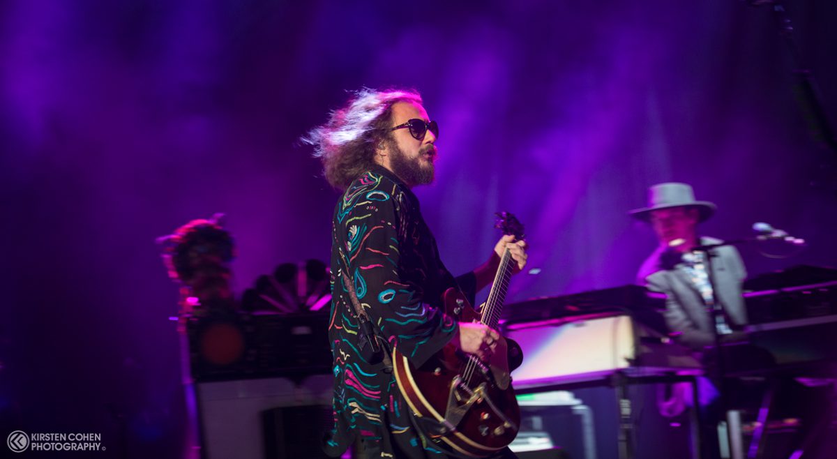 Musician playing guitar on stage with band.
