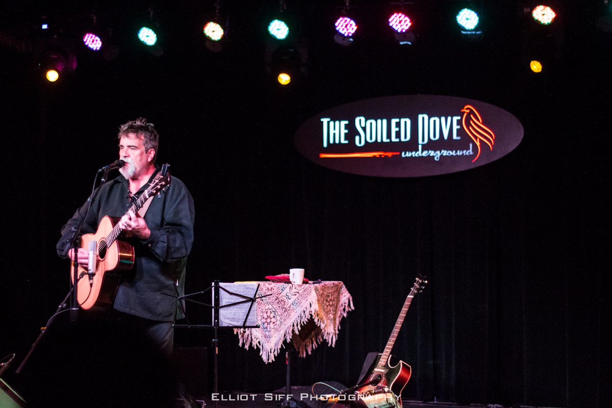 Musician performing on stage with guitar.