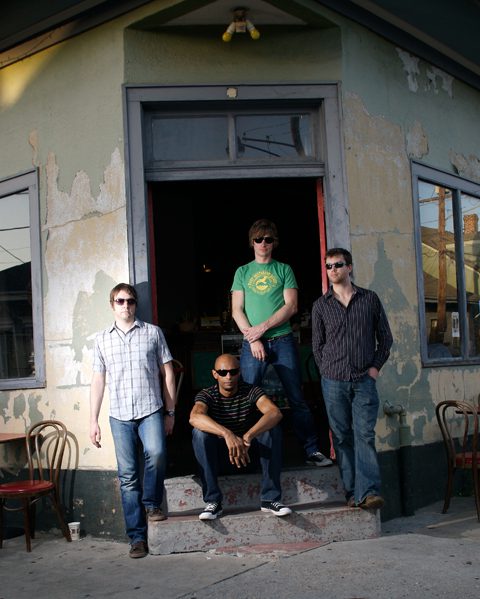 Four men posing outside a rustic building.