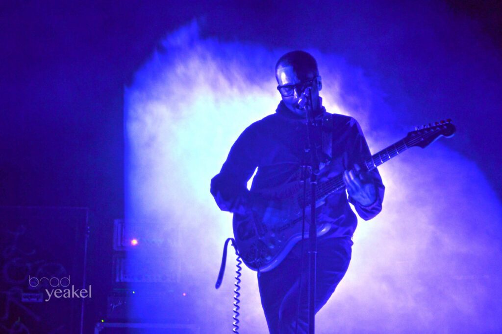 Guitarist performing on stage with blue lighting.