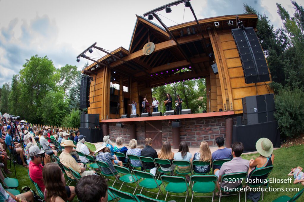 Outdoor concert with audience and wooden stage.