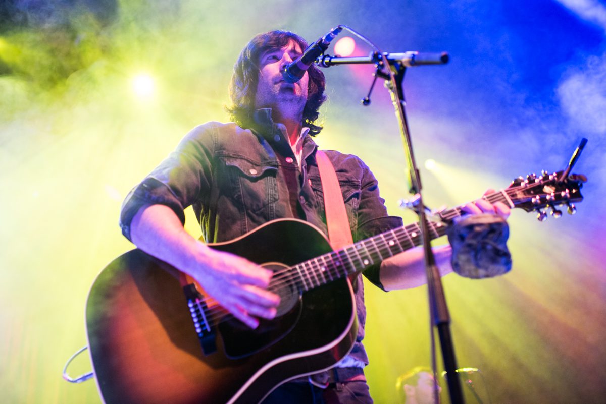 Musician playing guitar under colorful stage lights.