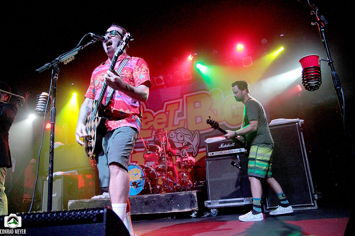 Band performing energetically on colorful stage.