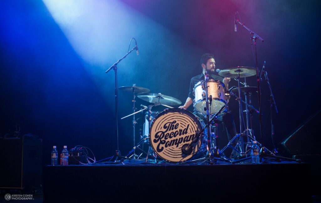 Drummer performing on stage with blue lights.