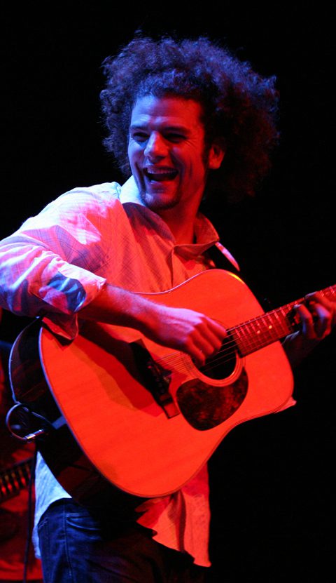 Musician joyfully playing acoustic guitar on stage.