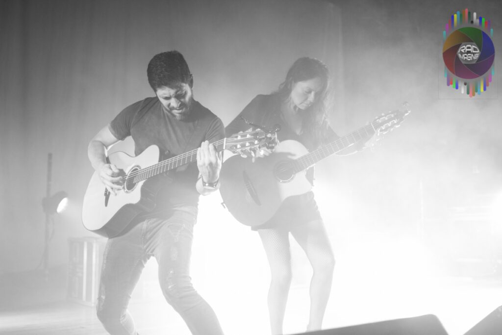 Musicians playing guitars on stage, dramatic lighting.