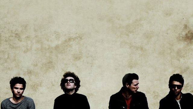 Four people sitting against a textured wall.