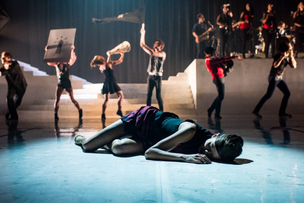 Dancer on stage with performers in background.