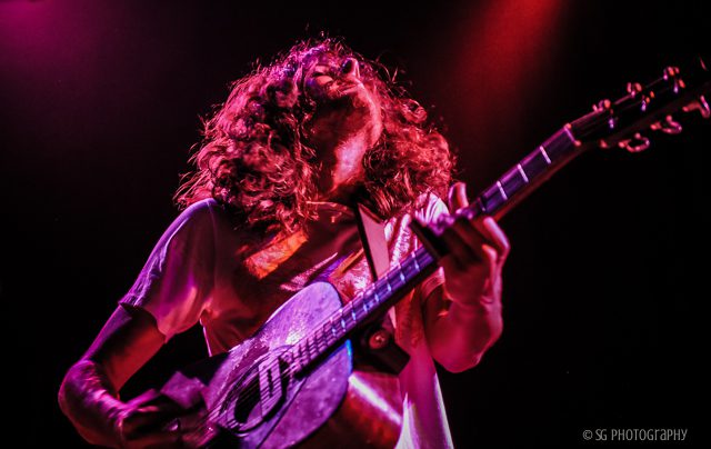 Musician playing guitar under colorful stage lights.