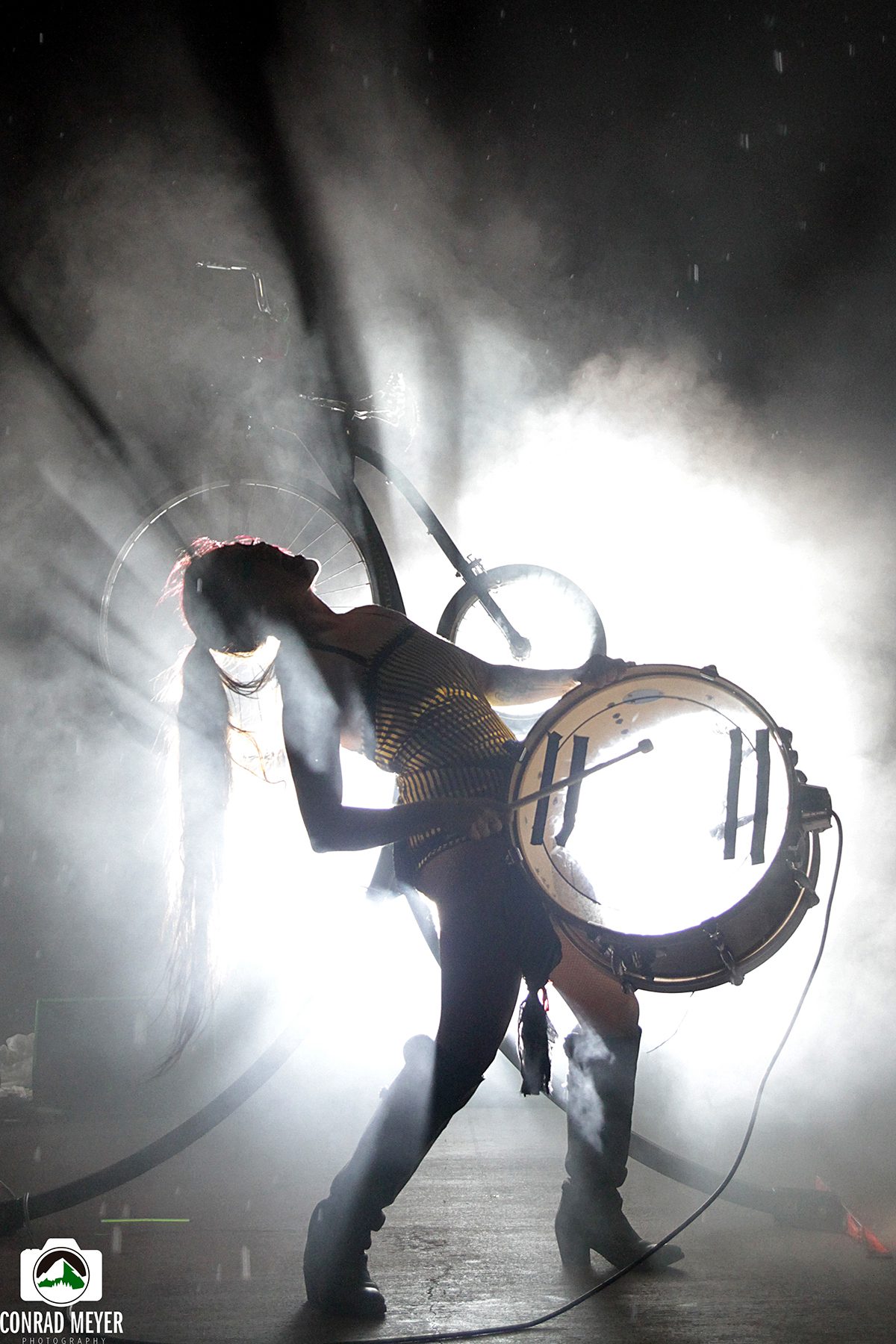 Performer with drum silhouetted against bright light.
