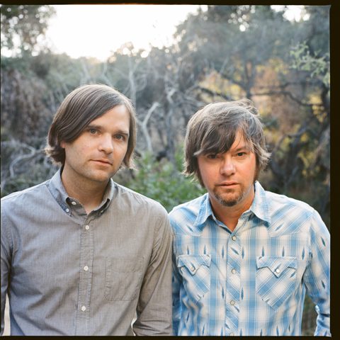 Two men standing outdoors in casual shirts.