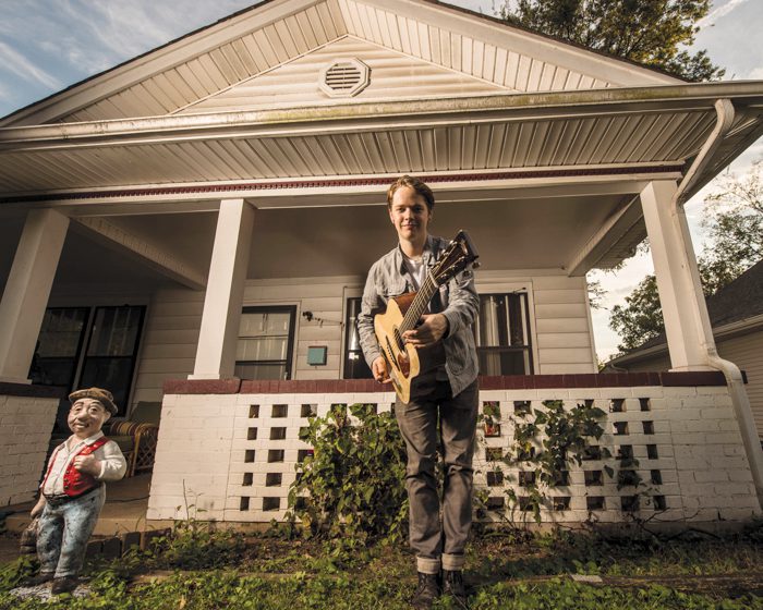 Man playing guitar in front of house.