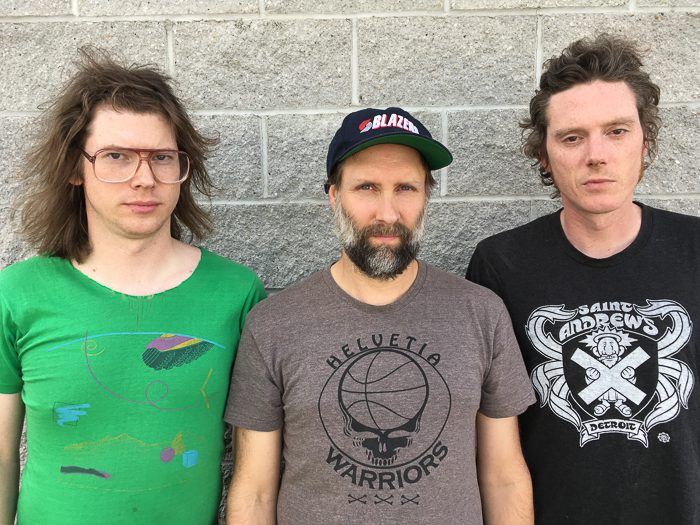 Three men standing against a brick wall.